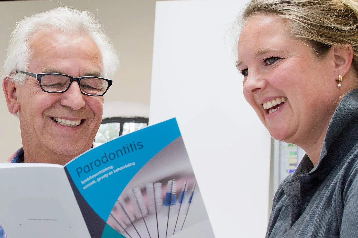 Een lachende patiënt leest een folder over parodontitis bij Moai Tandzorg